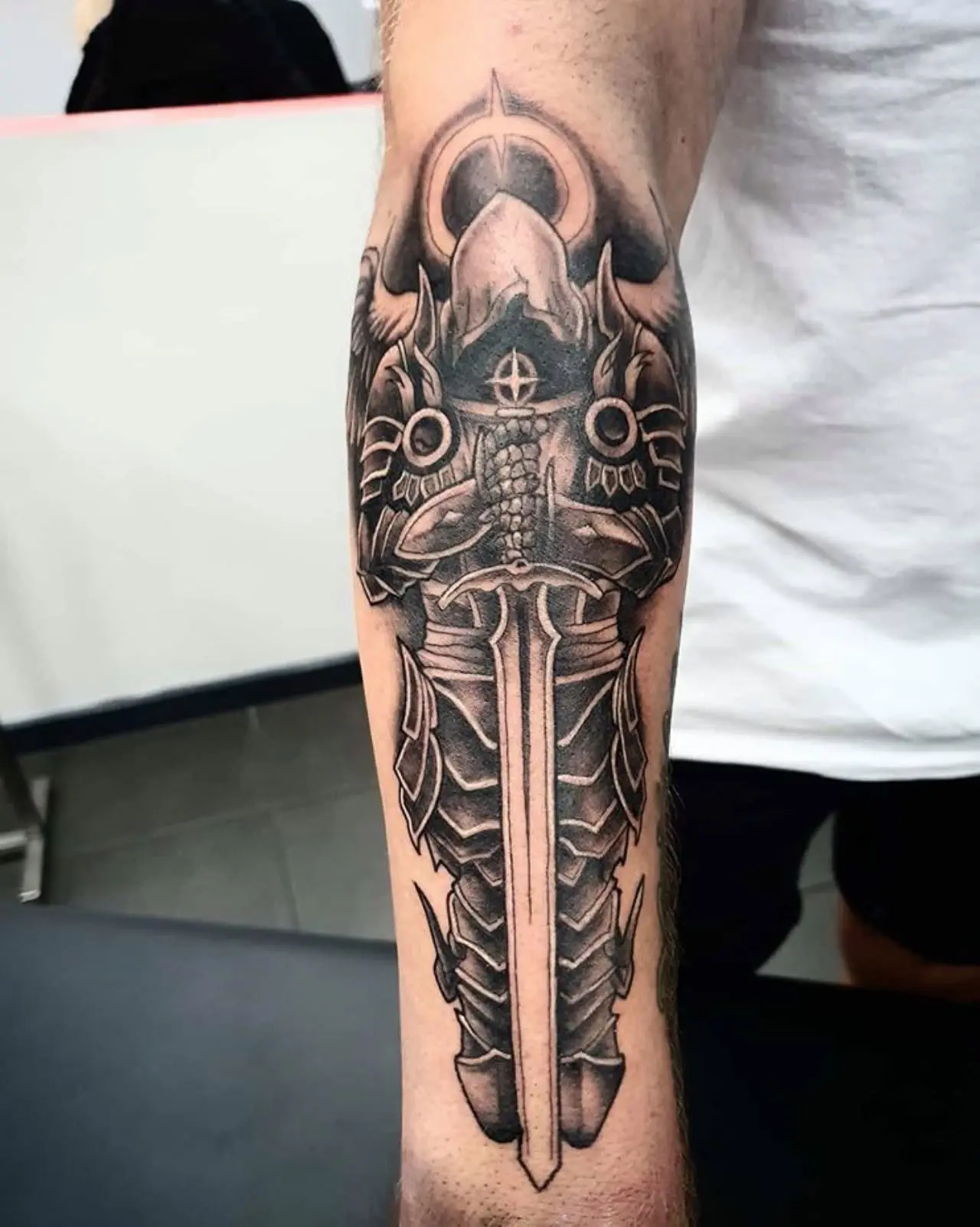 Black and grey armoured angel holding a sword down the length of a forearm