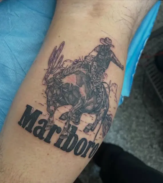 Black and grey cowboy on a bucking horse above the word Marlboro on a forearm