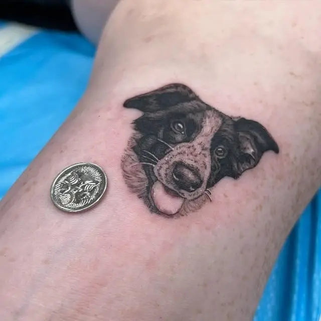 Small realistic dog portrait tattoo photographed beside a coin for scale