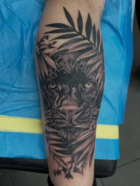 Black panther face framed by palm leaves on a forearm